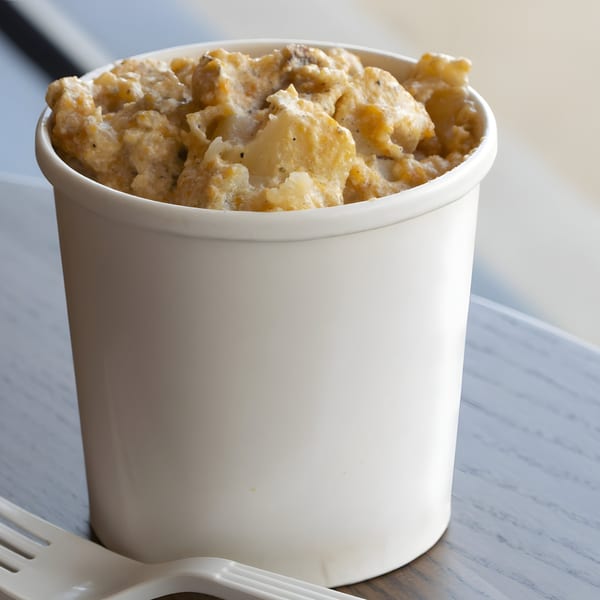 Creamy mac and cheese in a white paper cup with a plastic fork on a wooden table.