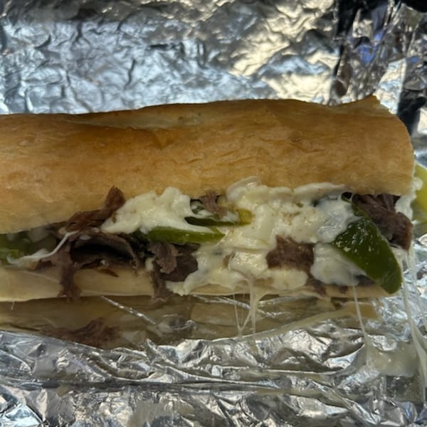 Doctor Dogs' cheesesteak with melted cheese, steak, and green peppers on a hoagie roll, wrapped in foil.