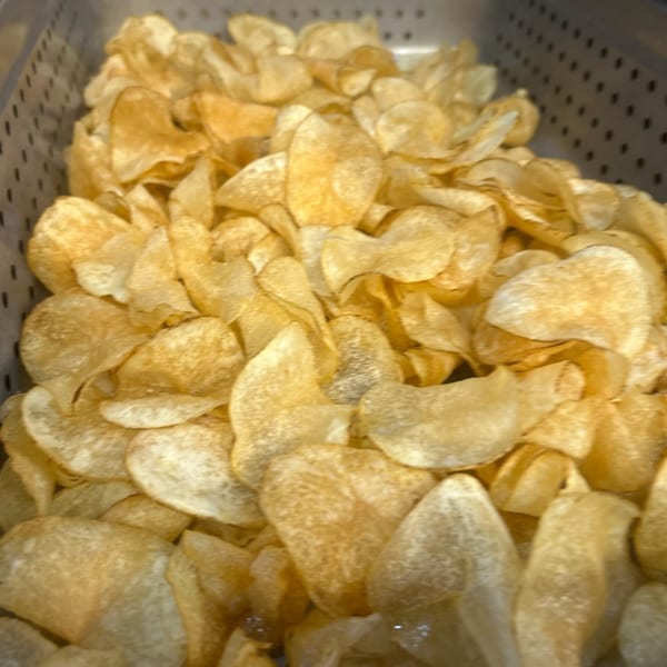 A close-up of a large quantity of golden-brown potato chips in a metal container.