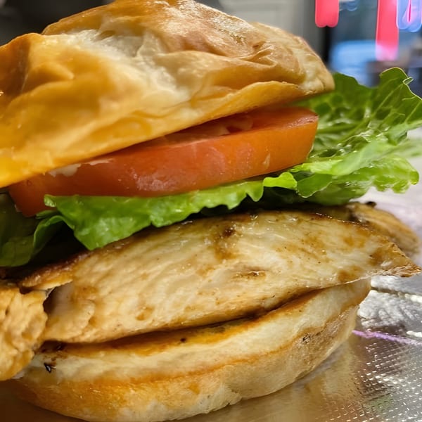 Grilled chicken sandwich with lettuce and tomato on a toasted bun, served on foil.