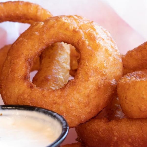 Close-up of golden-brown, crispy onion rings with a side of creamy dipping sauce.