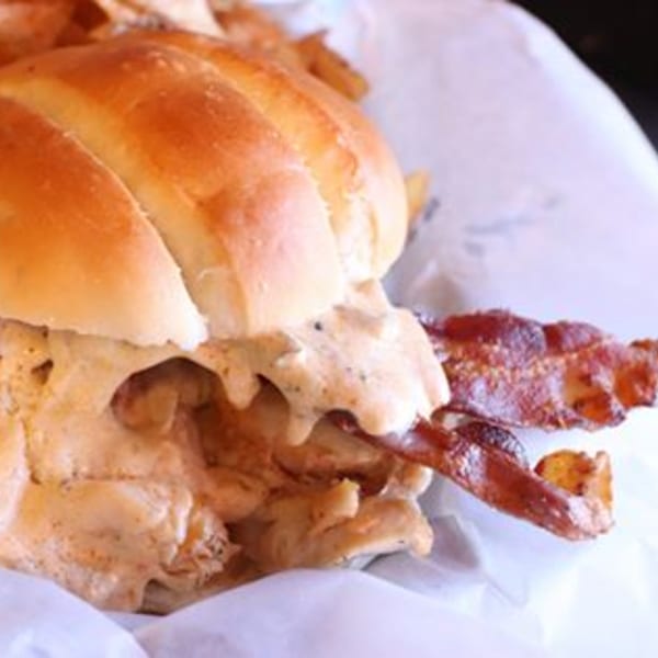 A Doctor Dogs sandwich with creamy filling and crispy bacon on a bun, served with fries.