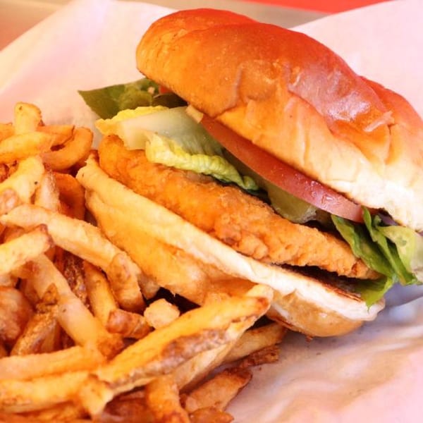 A crispy chicken sandwich with lettuce, tomato, and pickles, served with a side of golden fries.